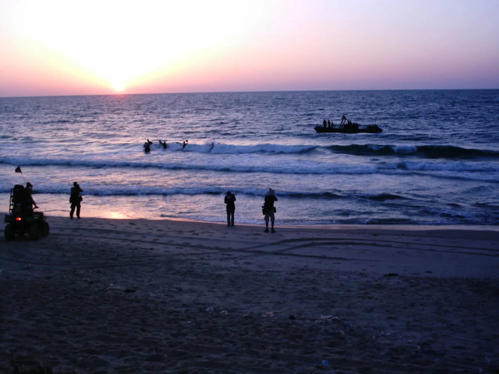 People and a small boat in the sea at sunset