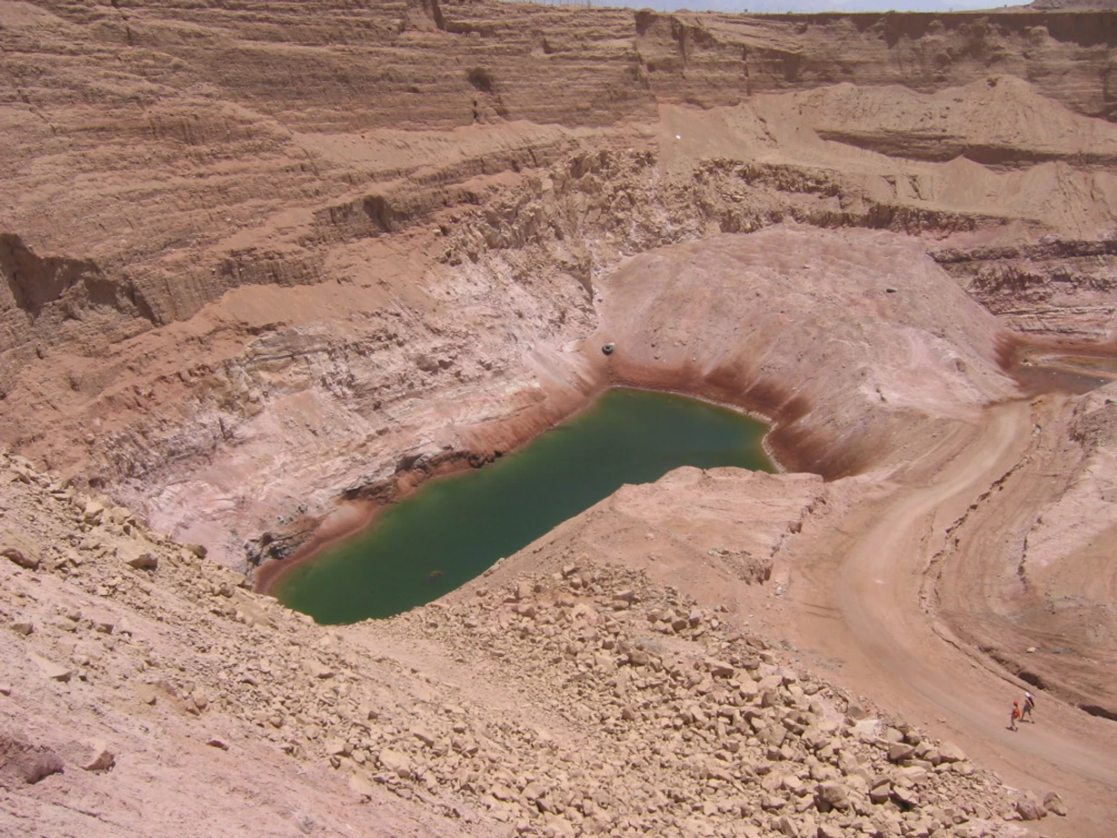 A small green pool at the bottom of a rocky desert excavation