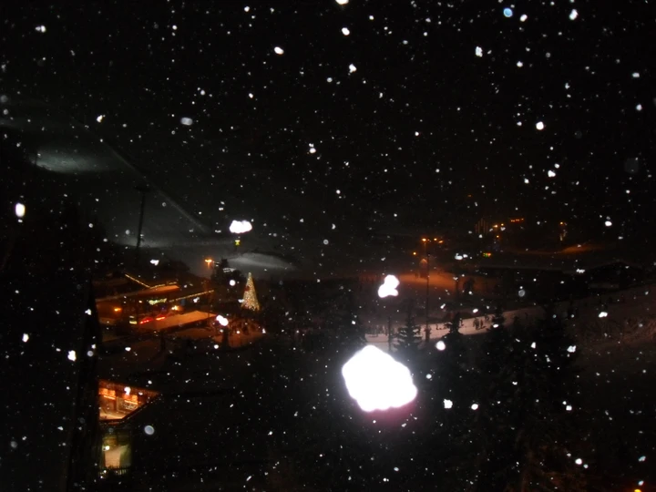 Heavy snow seen through a window at night, with ski resort lights below